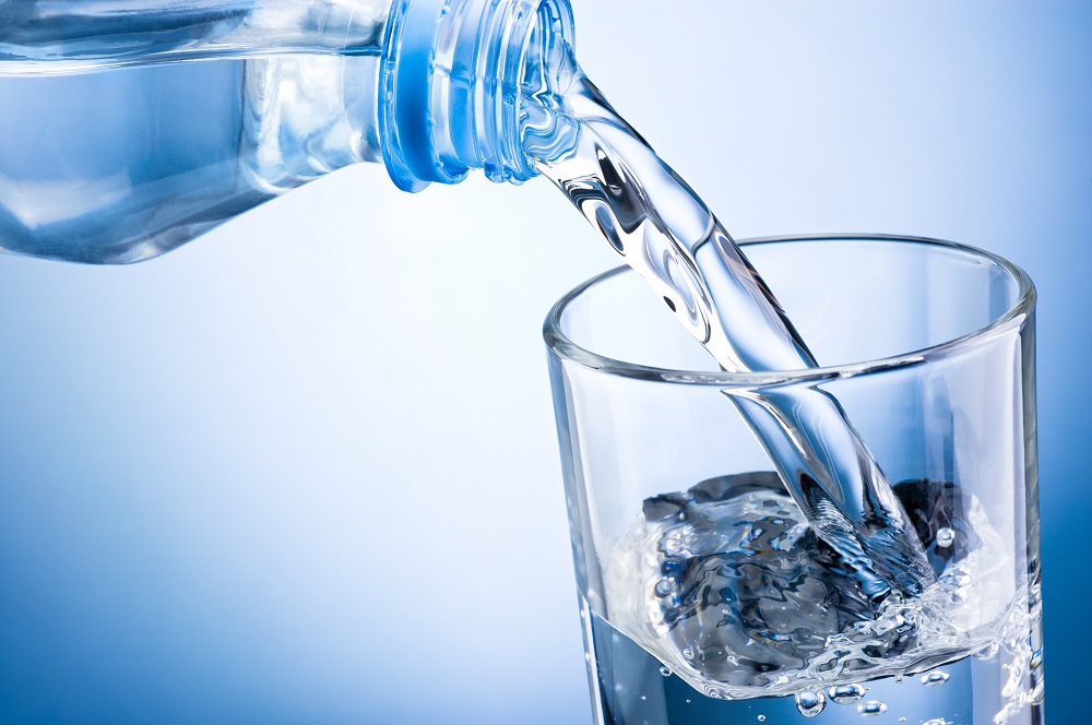 Close-up pouring water from bottle into glass on blue background