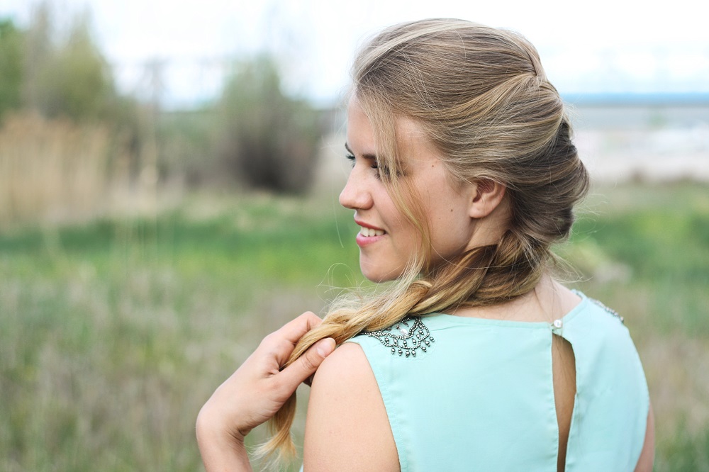 young beautiful blond girl smiling and  holding in hand natural hair in braid outdoor spring summer day