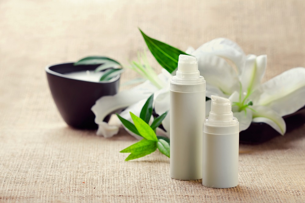 Face/body care concept: bottles of creams/lotions/serums with white lily flowers, closeup shot