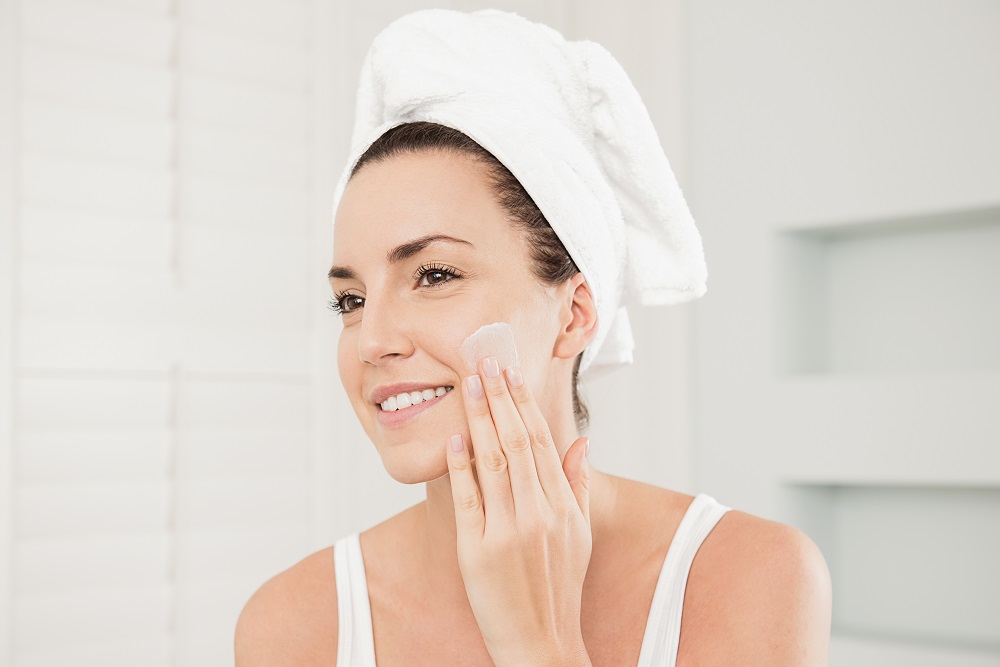 Lady in bathroom applying face cream to her cheek