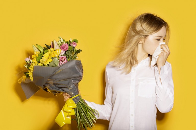 Lady on a yellow background with hay fever symptoms with a bouquet of flowers in her hand