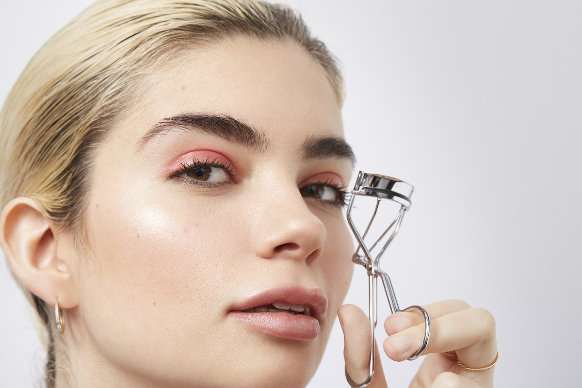 Young female holding eye lash curlers to her face