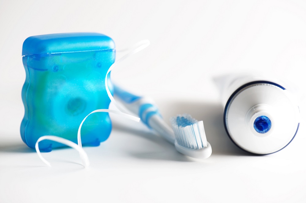 Image of dental floss, toothbrush and toothpaste on white surface