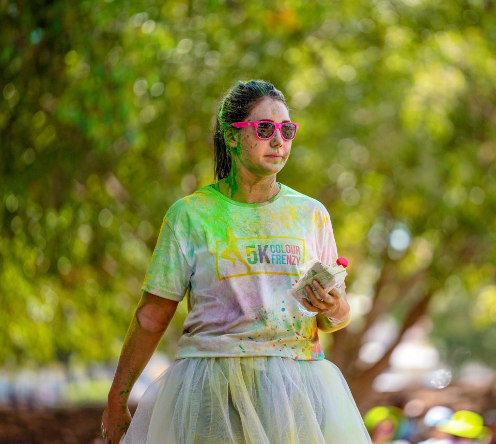 Female wearing pink sunglasses in a park splatted with colour from colour run