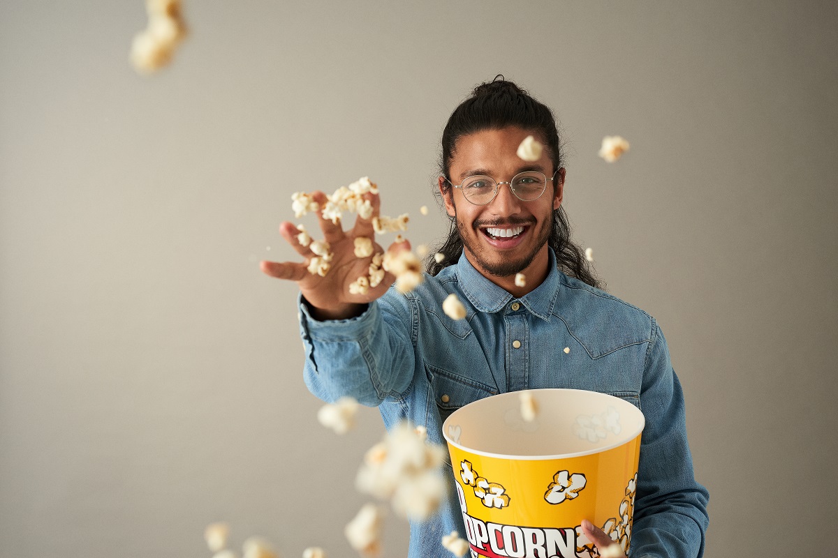 Male throwing popcorn at the camera with glasses on