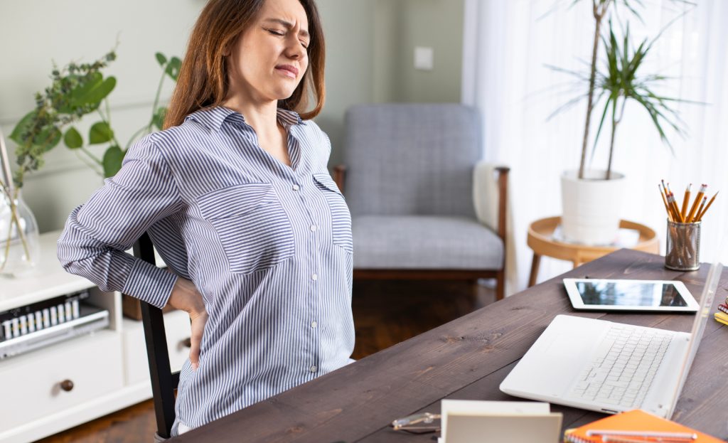 Woman sitting at a desk, holding her back in pain