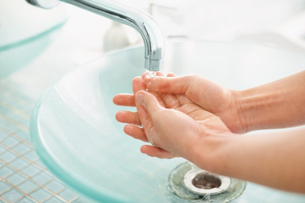 Detail view of a woman's hands under running water at sink