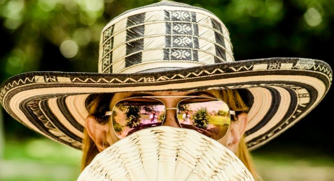 Female wearing sunglasses and a hat, hiding behind a fan