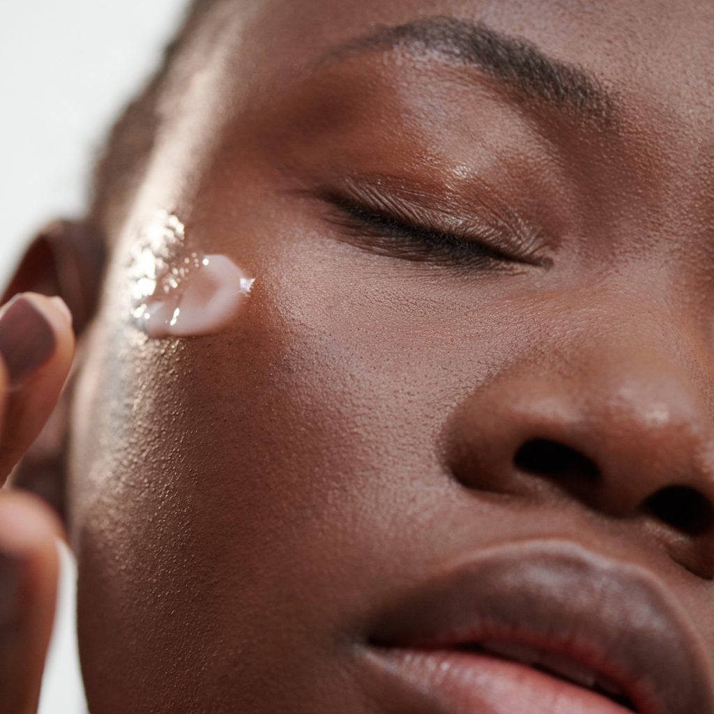 Black female applying serum to cheek with eyes closed