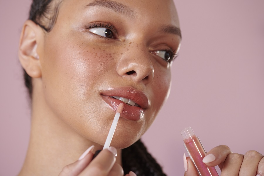 Woman applying a pink lip gloss whilst smiling