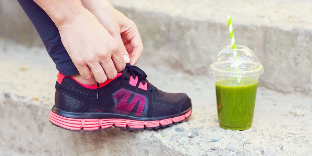 Green detox smoothie cup and woman lacing running shoes before workout. Fitness and healthy lifestyle concept