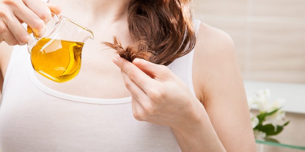 Unrecognizable woman applying oil mask to hair tips in a bathroom; beauty and haircare concept