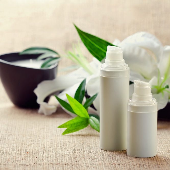 Face/body care concept: bottles of creams/lotions/serums with white lily flowers, closeup shot