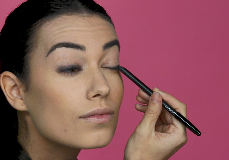 Woman applying kohl eyeliner to her eyelids with an eyeliner pencil