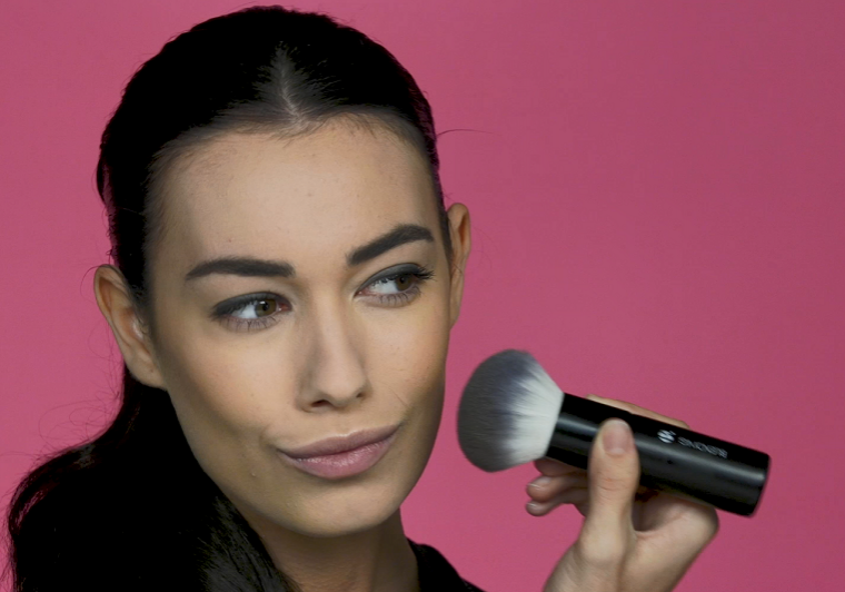 Woman applying bronzer to her cheeks with large makeup brush