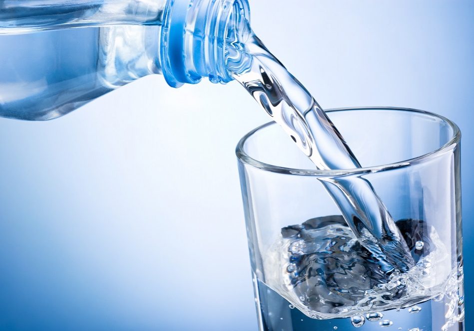 Close-up pouring water from bottle into glass on blue background